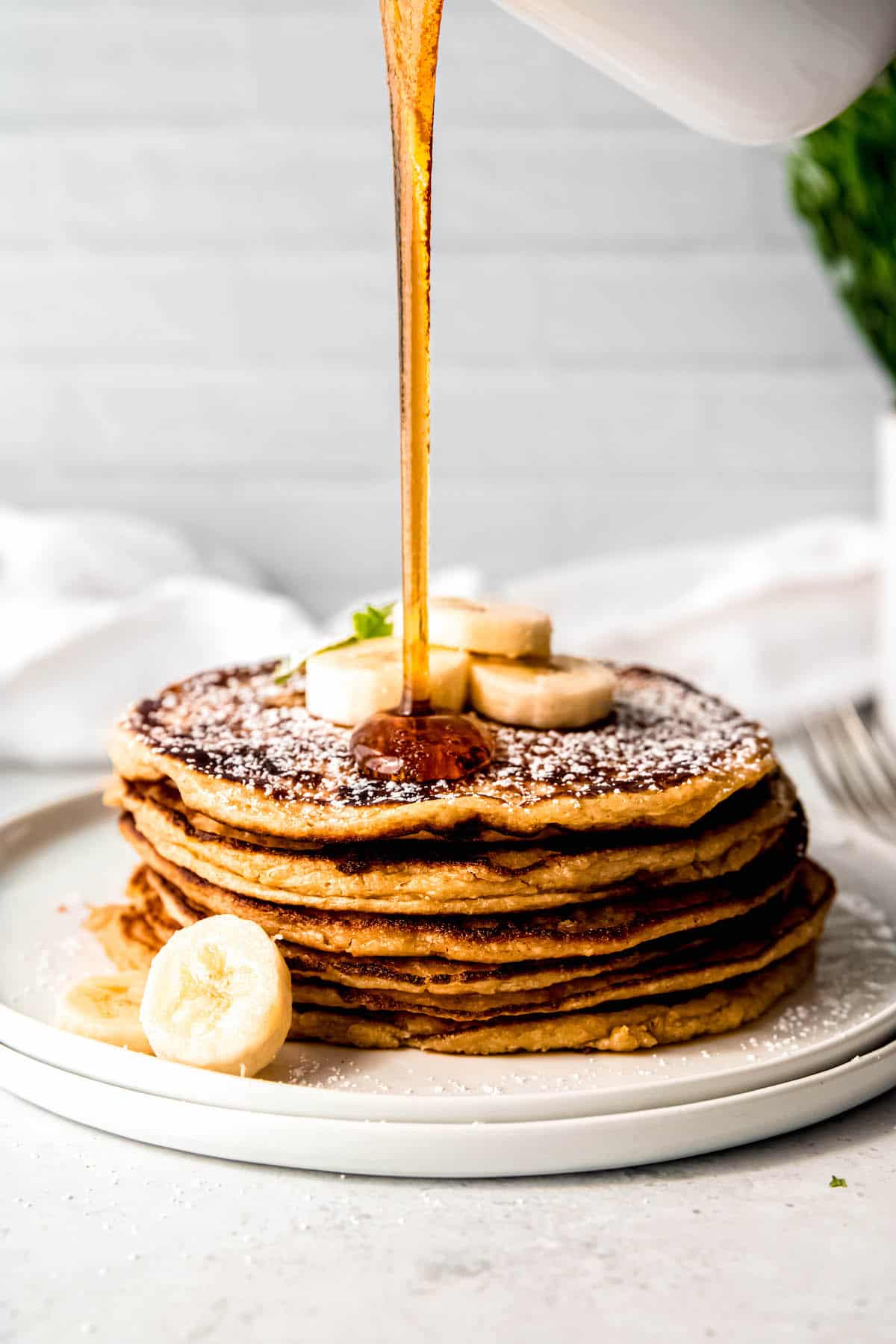 Action shot of maple syrup being poured on a stack of cottage cheese oatmeal banana protein pancakes.