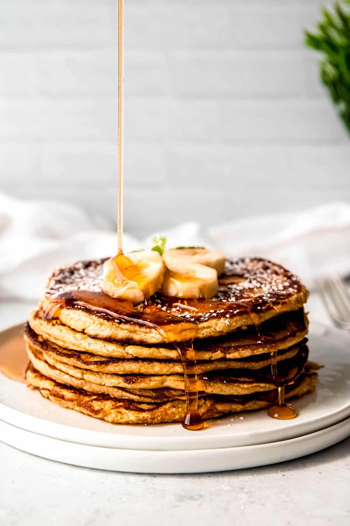 maple syrup spilling over a stack of oatmeal cottage cheese banana protein pancakes.