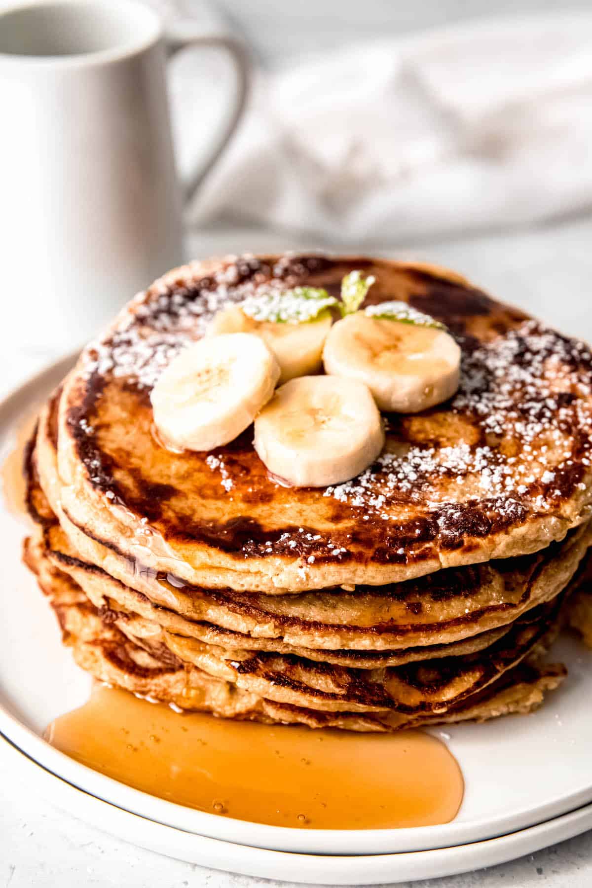 stack of banana protein pancakes made with cottage cheese and oats topped with bananas, maple syrup, and powdered sugar.