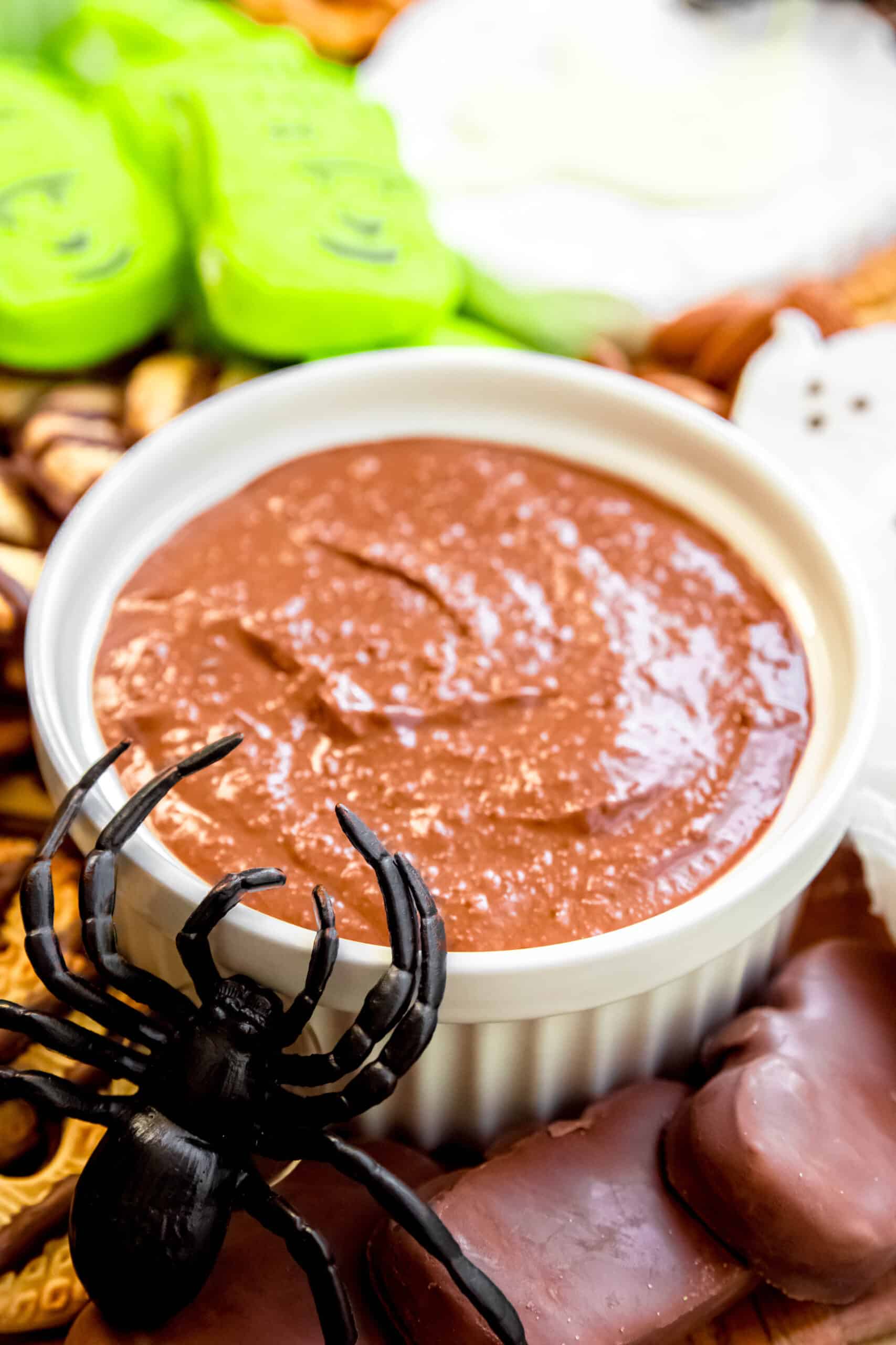 closeup shot of a plastic spider crawling into a dip next to pumpkin shaped peanut butter cups and Frankenstein marshmallows.
