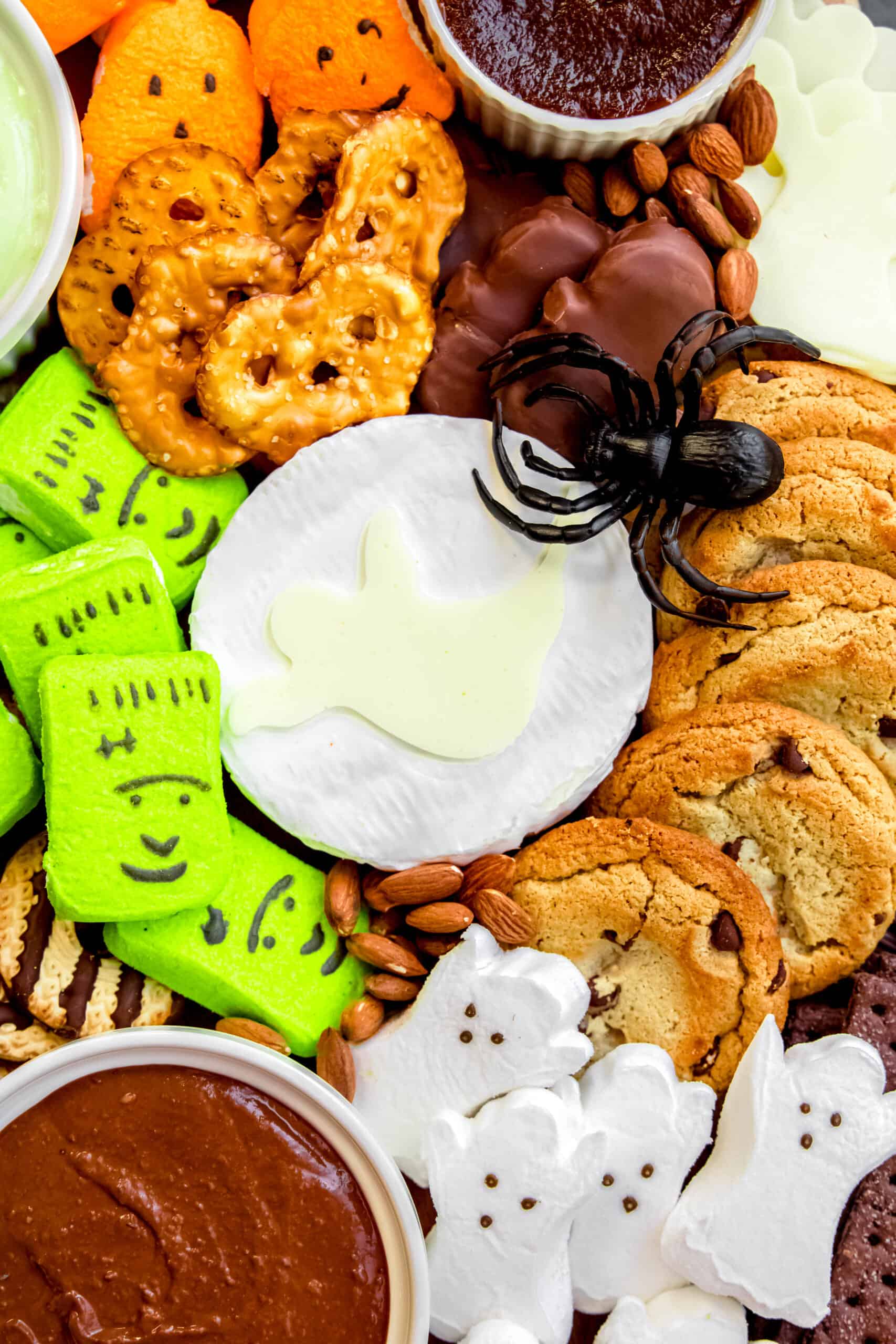 overhead shot of a round of brie with a cut out cheese ghost on top surrounded by pretzel thins, cookies, and spreads.