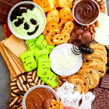 hand dipping a pretzel thin into chocolate hummus on the Halloween s'mores charcuterie board.