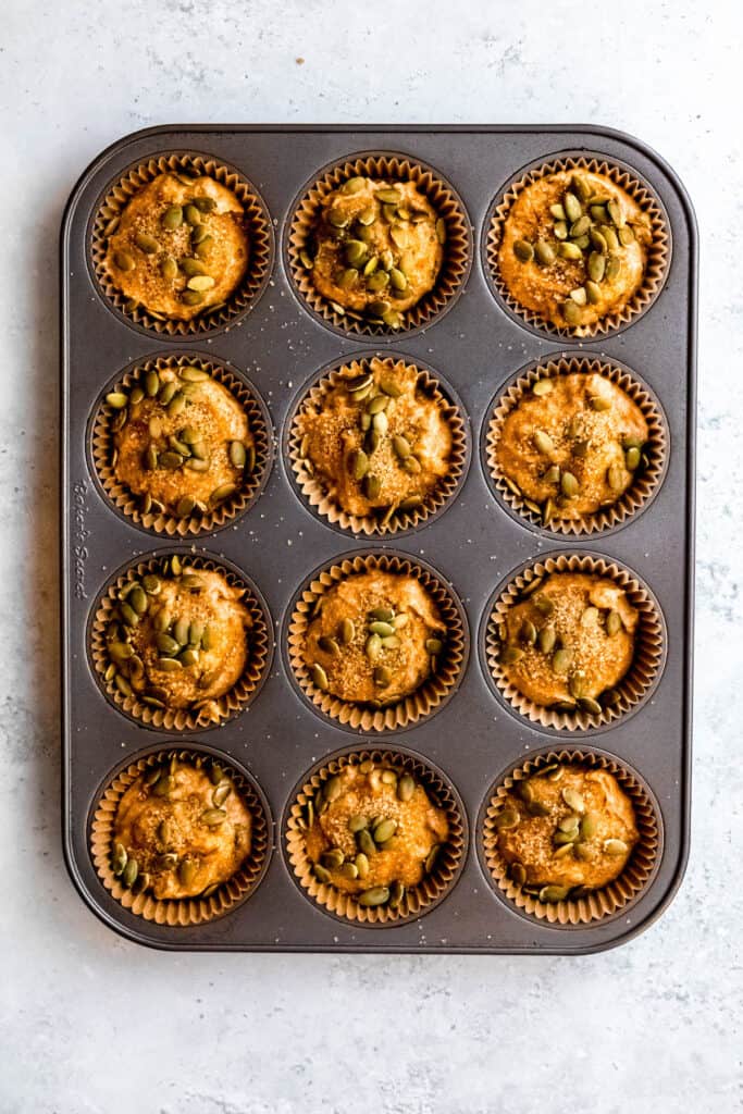 each unbaked muffin has been topped with pepitas and turbinado sugar.