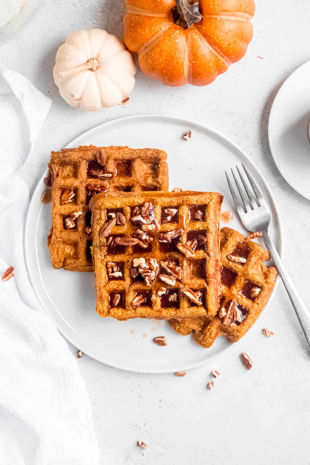 flat lay shot of 3 pumpkin pecan waffles on a white plate topped with spiced pumpkin pecan maple syrup.