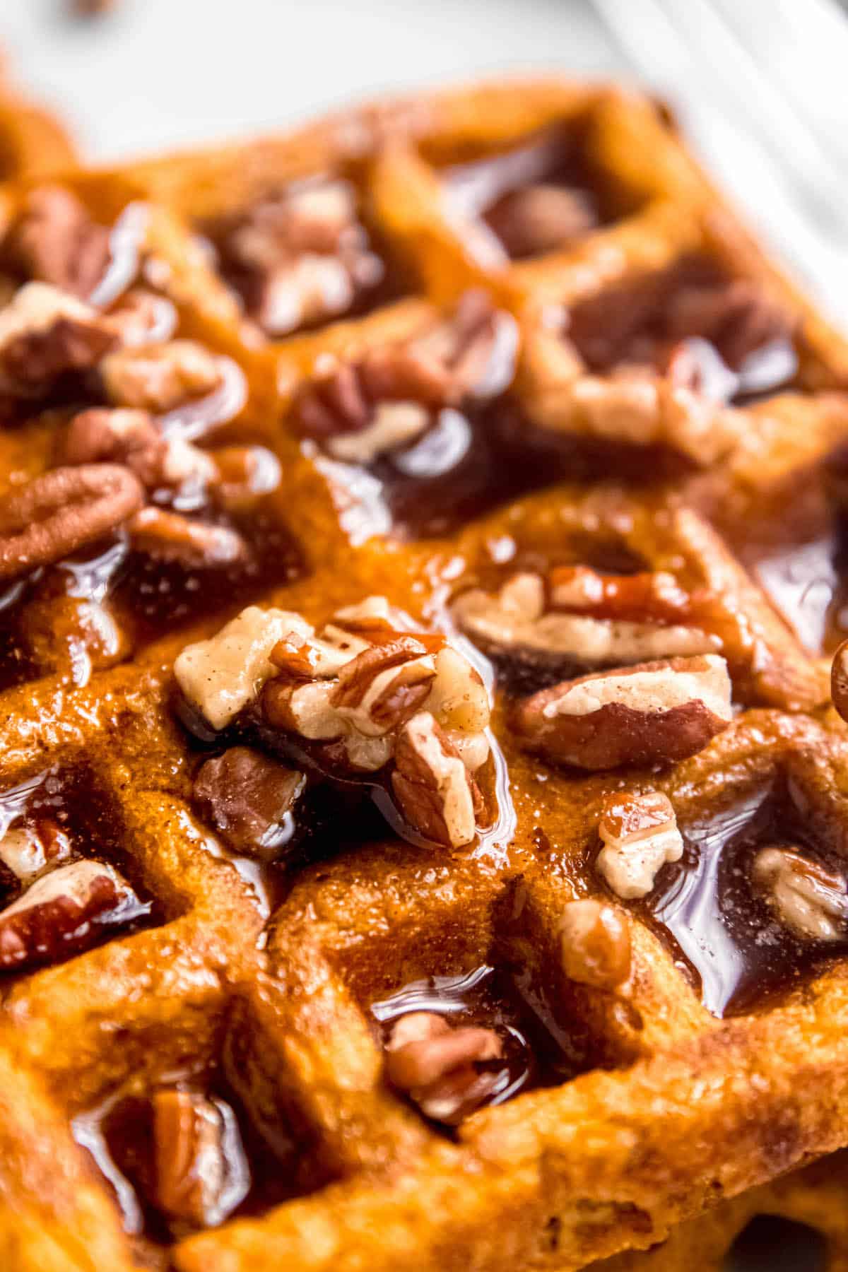 45 degree angle closeup shot of a pumpkin pecan waffle with the wells filled with pecan maple syrup.