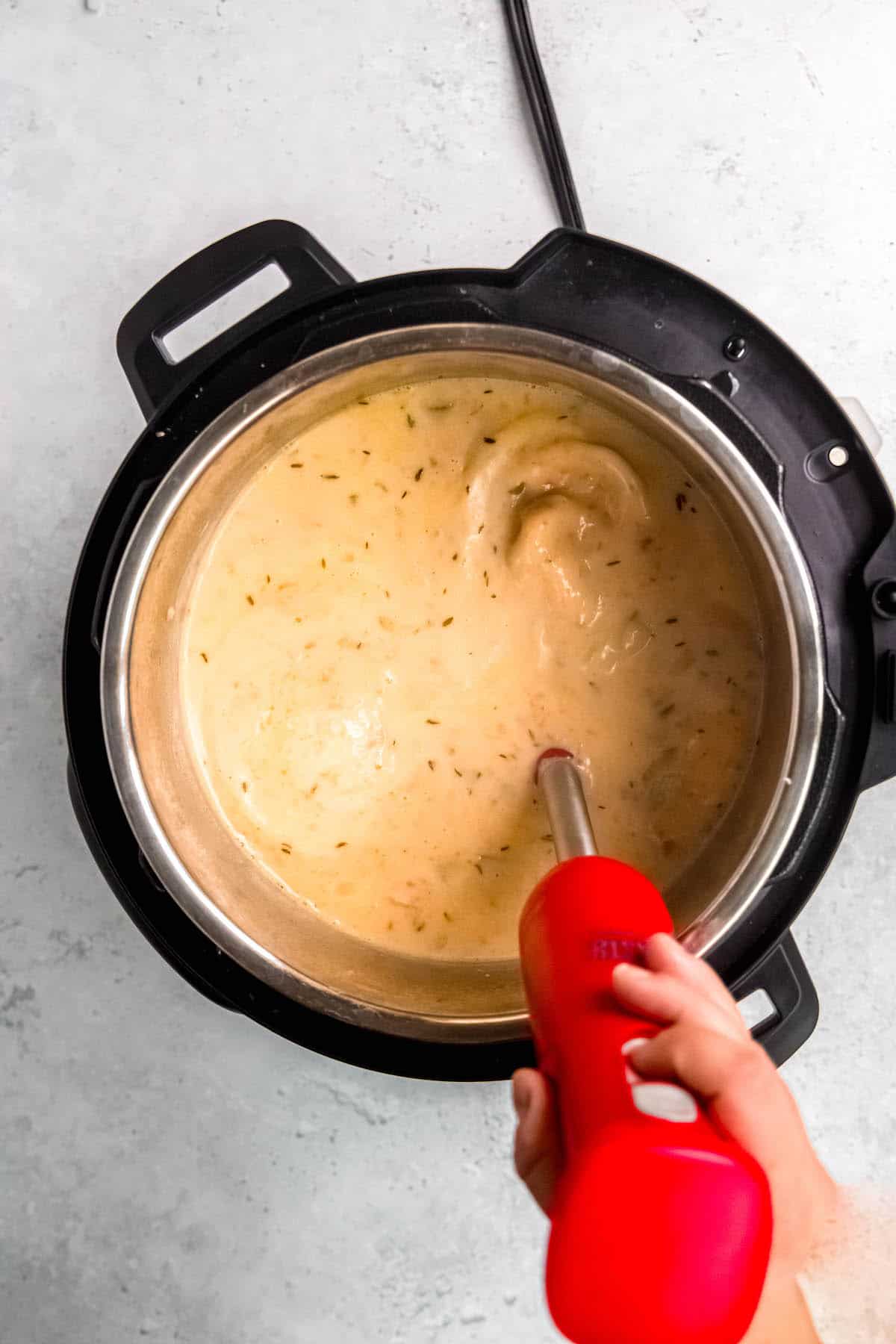 using an immersion blender to blend the potato soup in the instant pot.