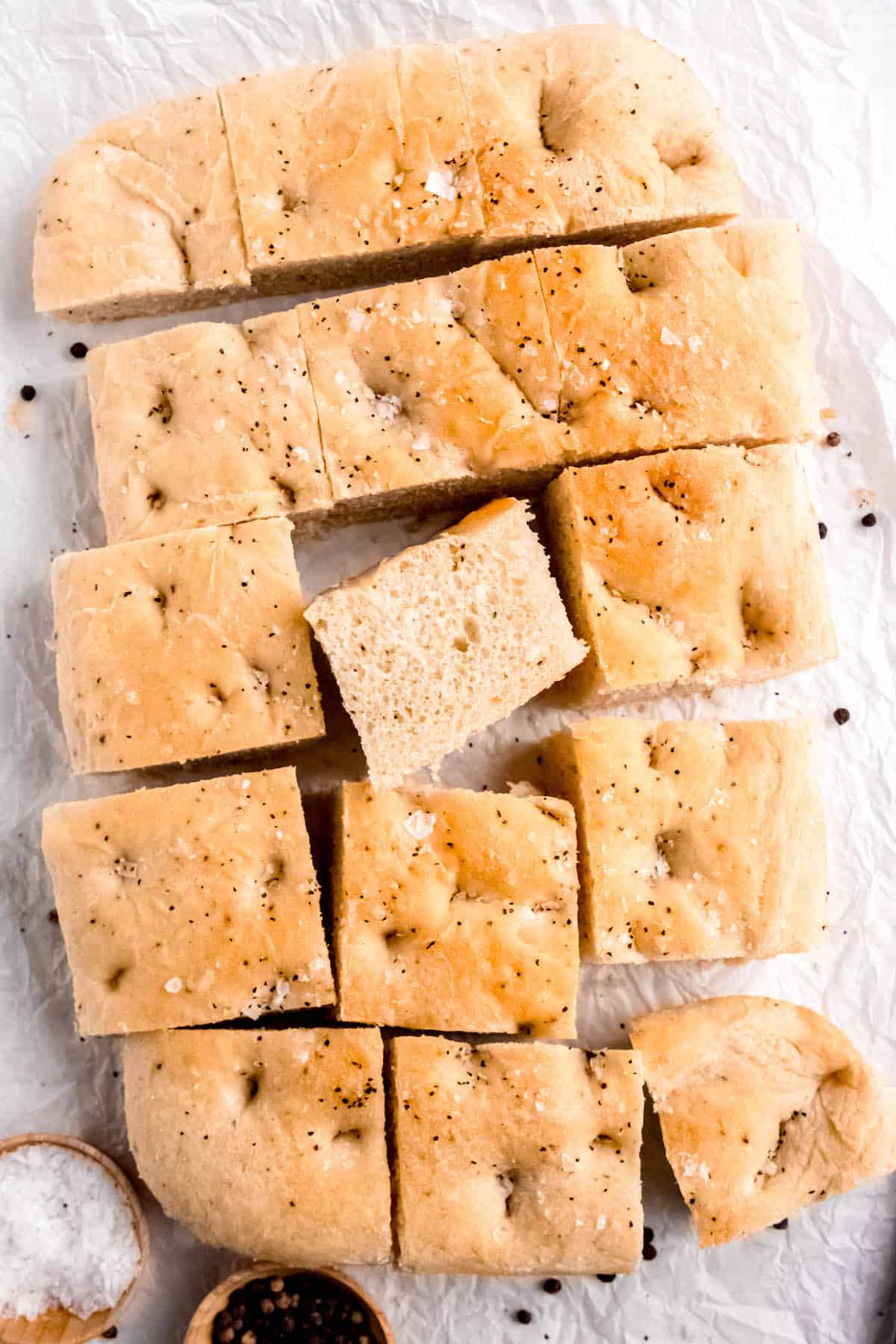 flat lay shot of the sliced loaf of black pepper focaccia with the middle slice turned on its side so you can see how thick and fluffy the bread is.
