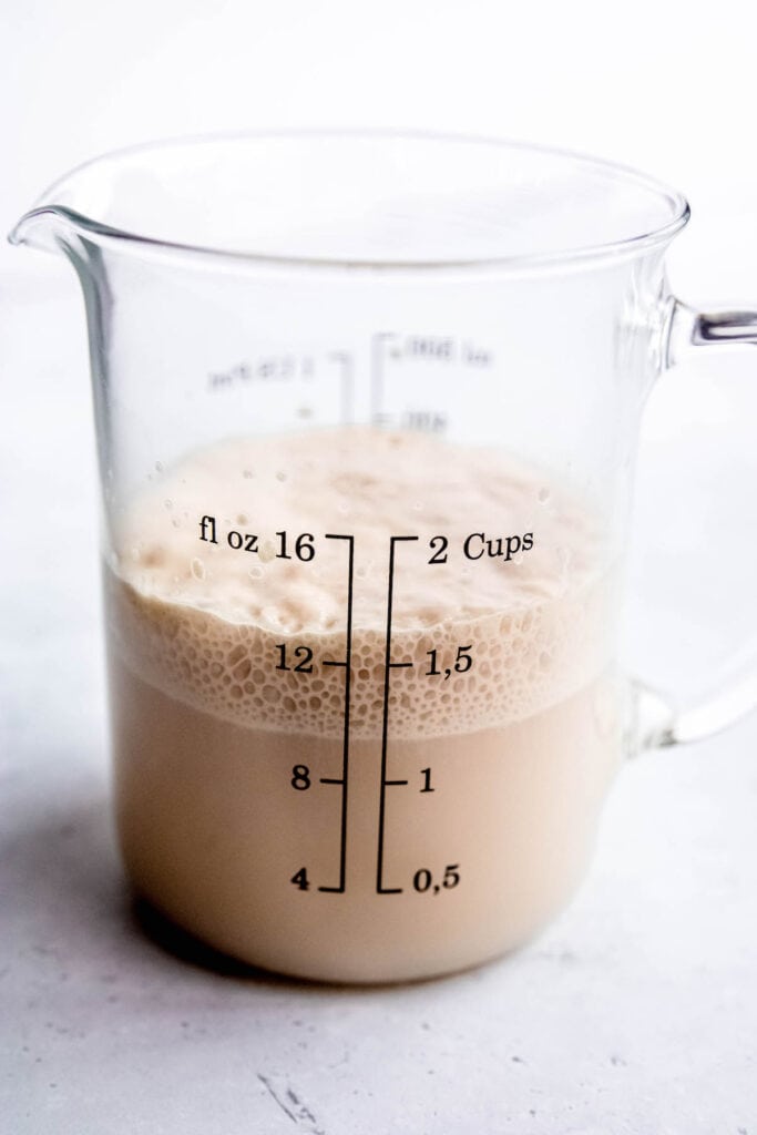 yeast mixture in a clear glass measuring cup showing a bubbly head on top of a tan liquid.