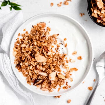 square hero image of a white bowl of yogurt topped with homemade vanilla almond granola.