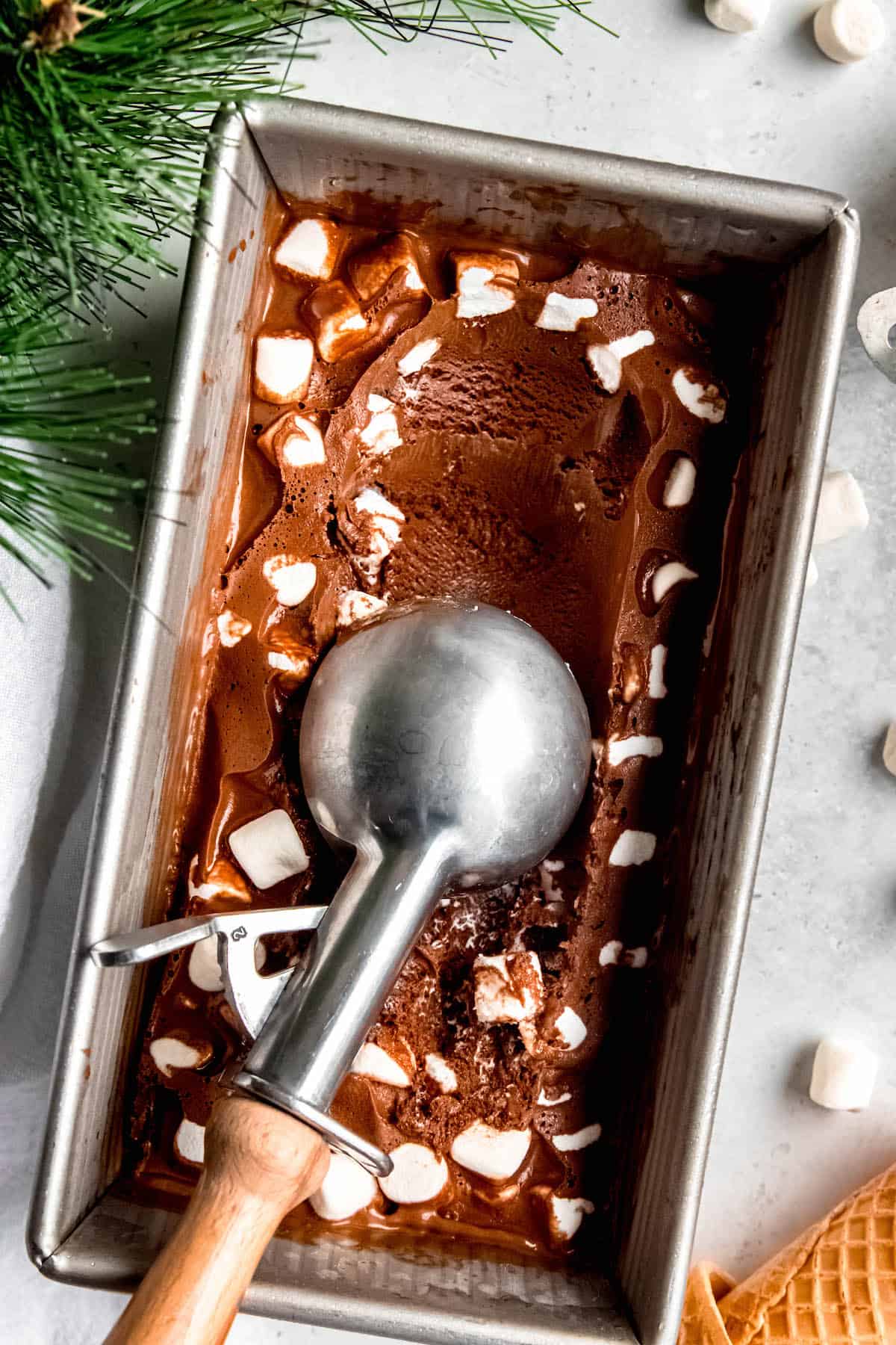 flat lay shot of a loaf tin of homemade hot chocolate marshmallow ice cream with an ice cream scoop having removed a serving.
