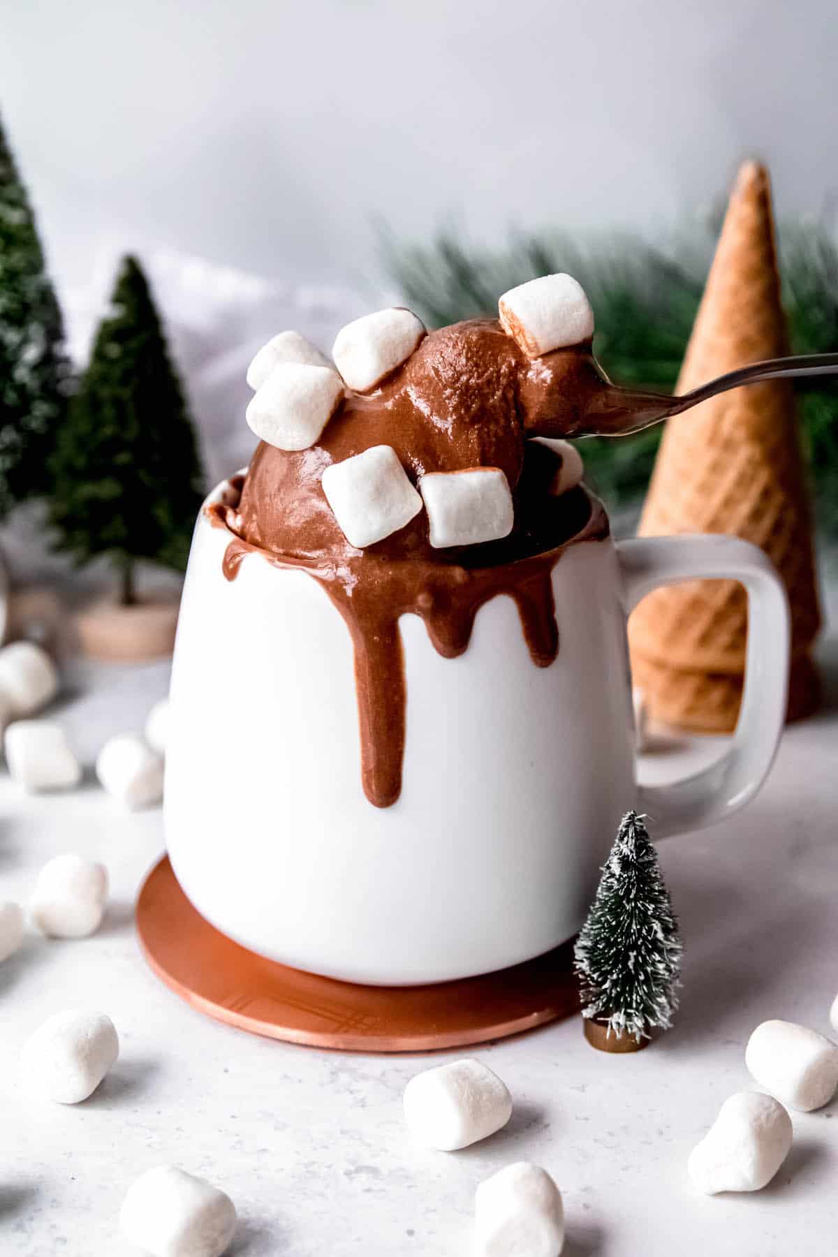 white mug filled with a scoop of chocolate marshmallow ice cream with a spoon pulling out a stretchy bite.