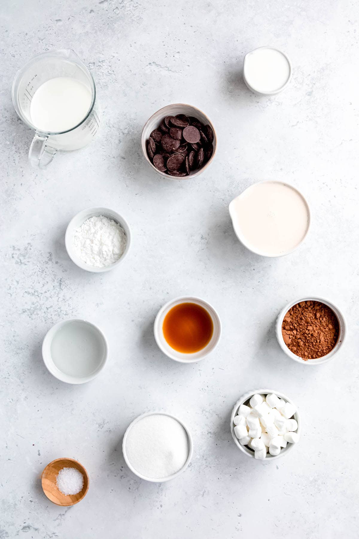 ingredients needed to make old fashioned homemade chocolate ice cream with marshmallows measured out in bowls on a white table.
