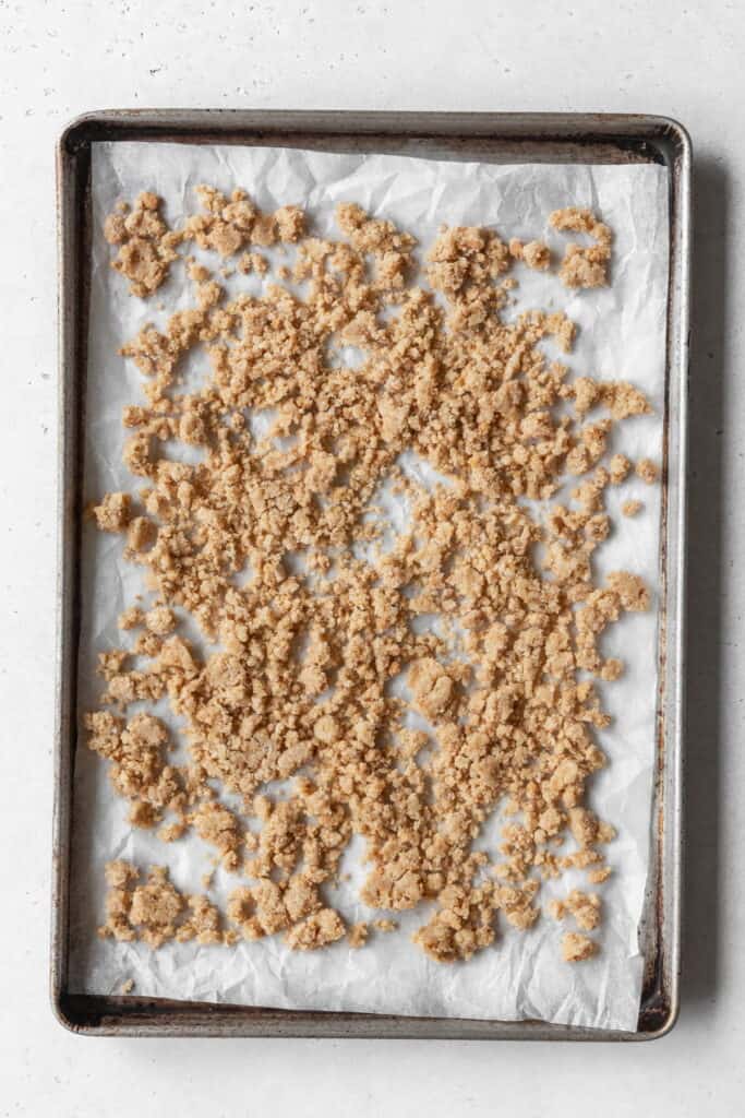 clumps of graham cracker crumble mixture spread out of a parchment-lined sheet pan.