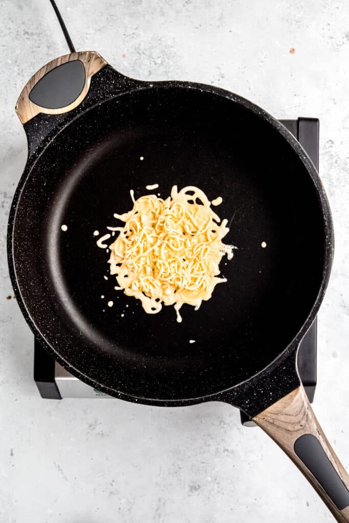 flat lay shot of grated gouda cheese in a non-stick skillet.