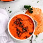 flat lay hero shot of a bowl of roasted red pepper soup with gouda frico on the side, garnished with fresh parsley.