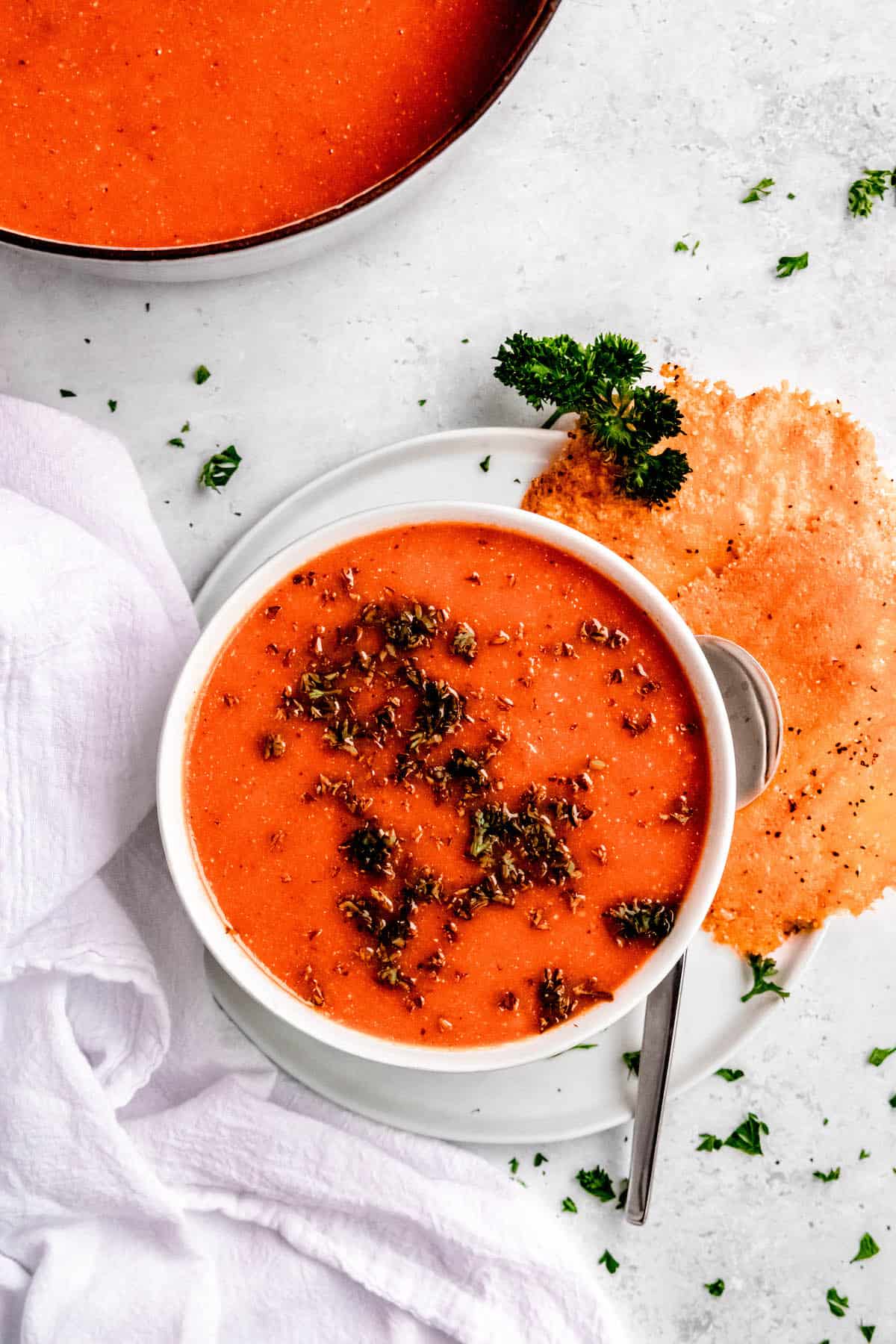 flat lay hero shot of a bowl of roasted red pepper soup with gouda frico on the side, garnished with fresh parsley.
