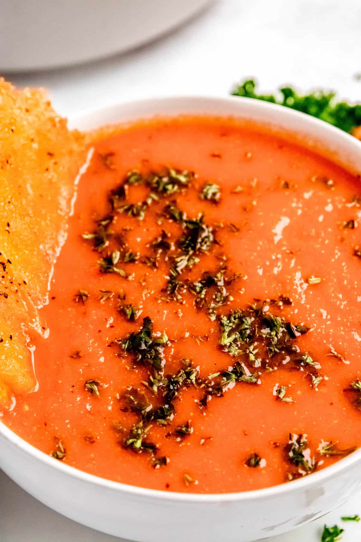 closeup shot of a bowl of roasted red pepper soup with gouda frico sticking out of the side.