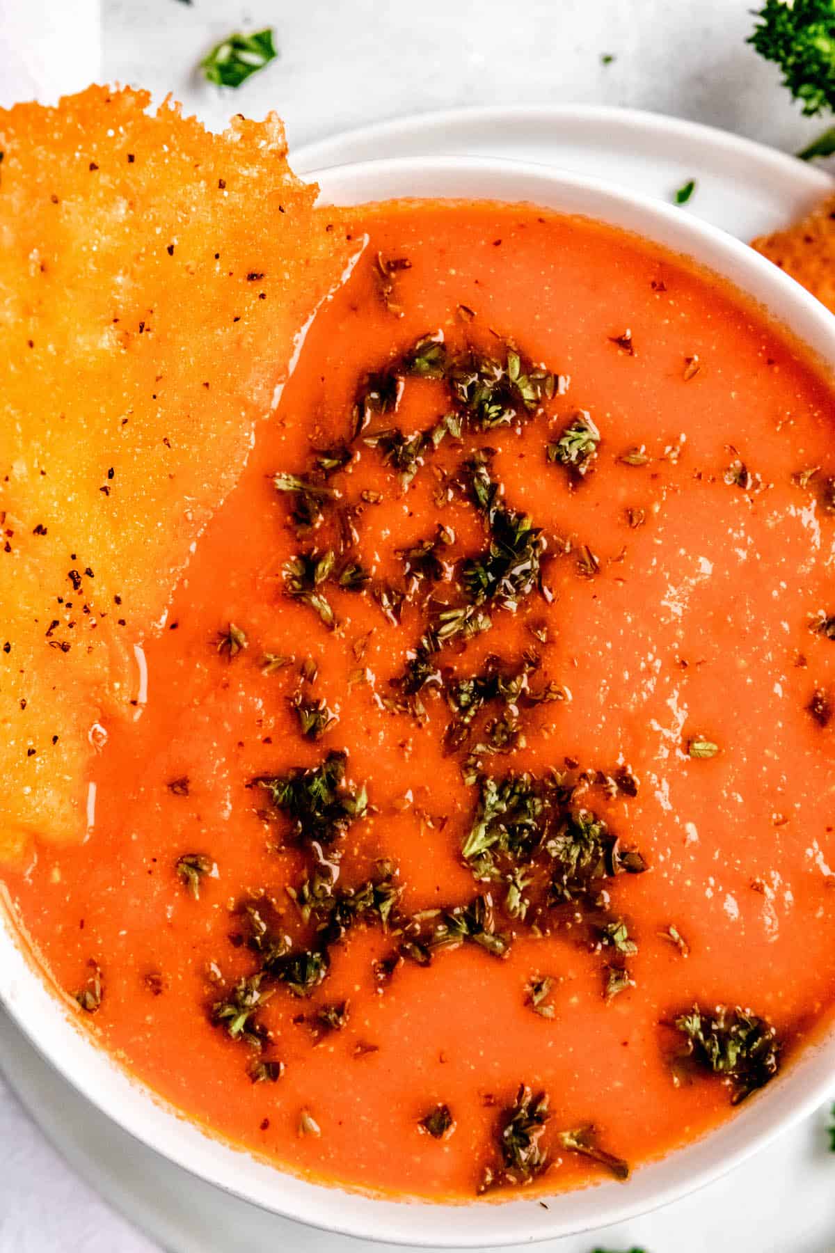overhead shot of a bowl of roasted red pepper soup with gouda frico and a parsley garnish.