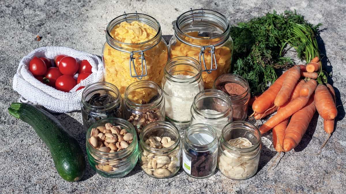 glass jars filled with dry ingredients nexxt to a bunch of carrots, a zucchini, and a small bag of cherry tomatoes.