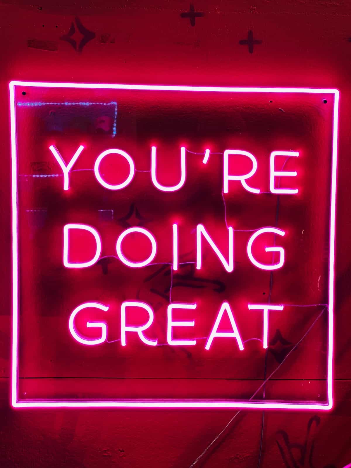 square pink neon light that reads "you're doing great."