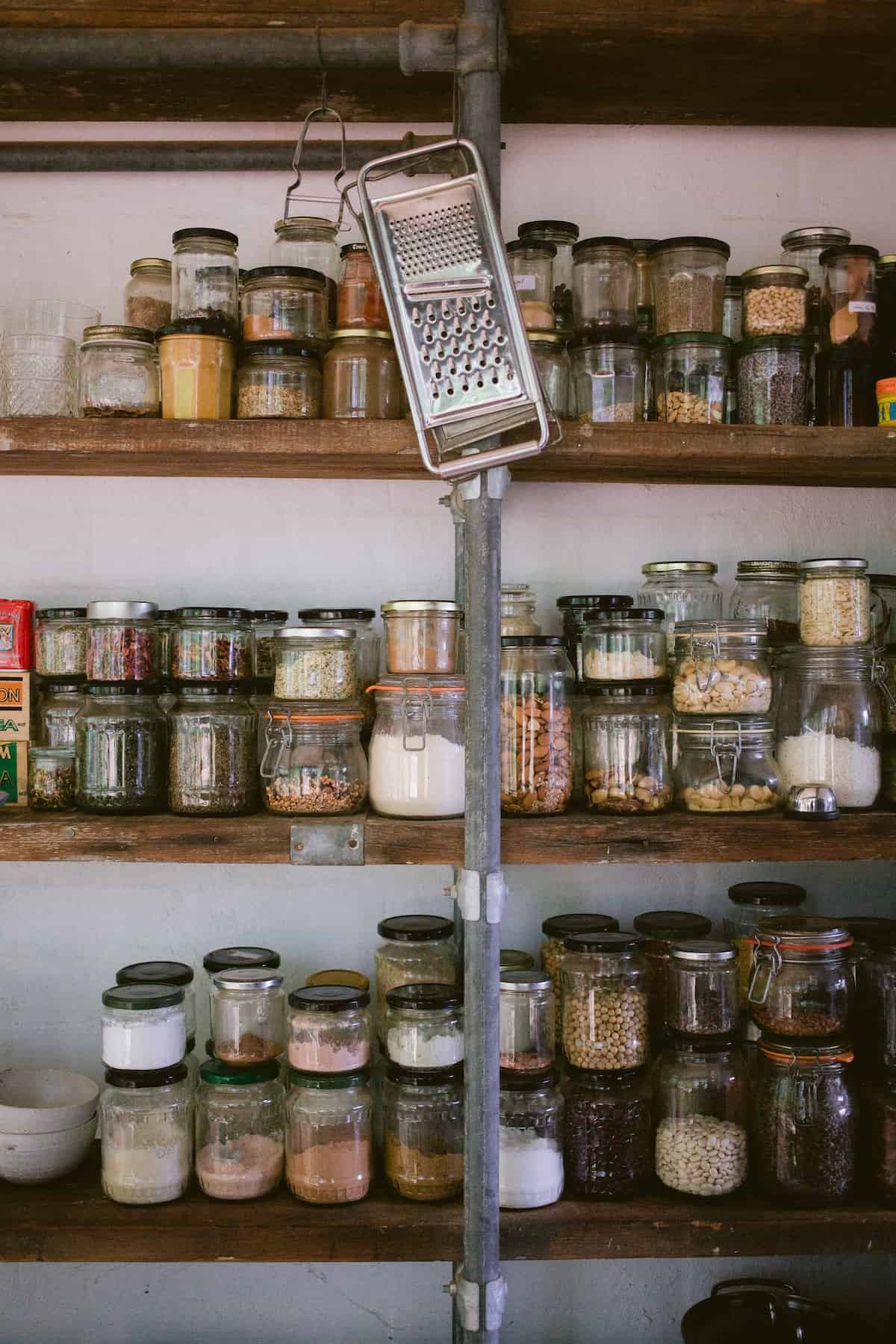 rustic wooden pantry shelves filled with glass jars filled with shelf-stable ingredients.