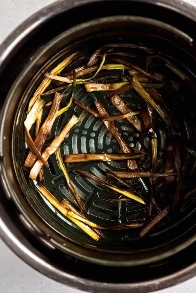 frizzled leeks in the bottom of an air fryer after turning deep mahogany brown.