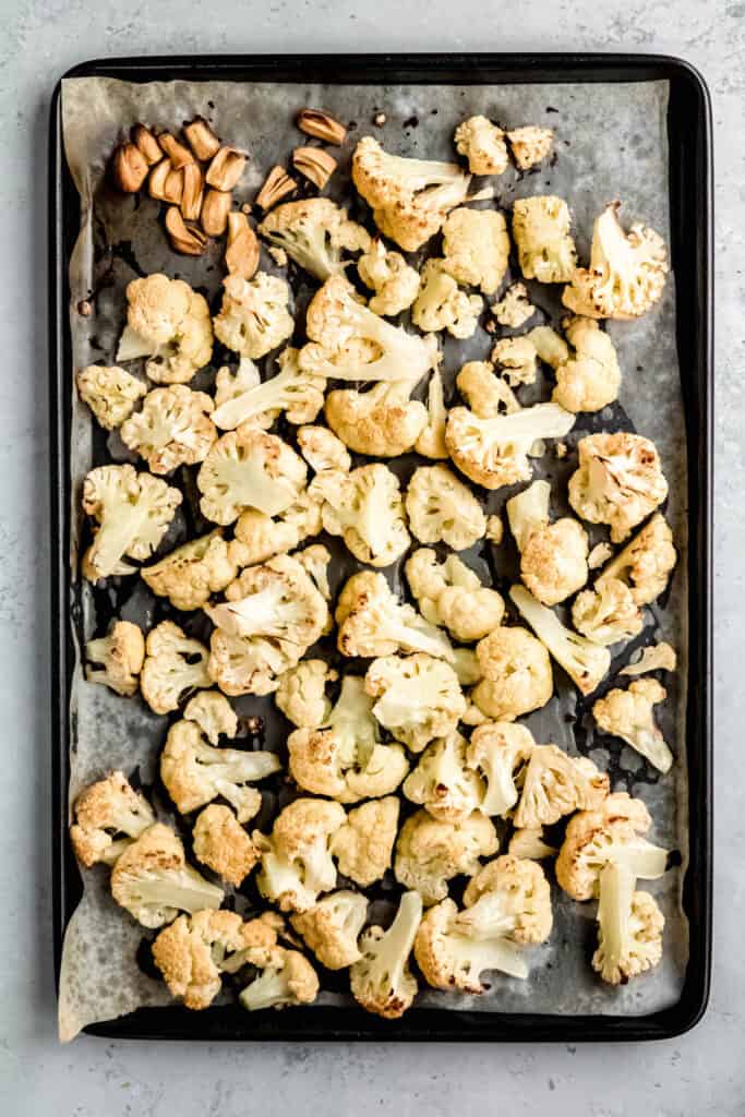 roasted cauliflower and golden garlic on a parchment lined sheet pan after coming out of the oven.