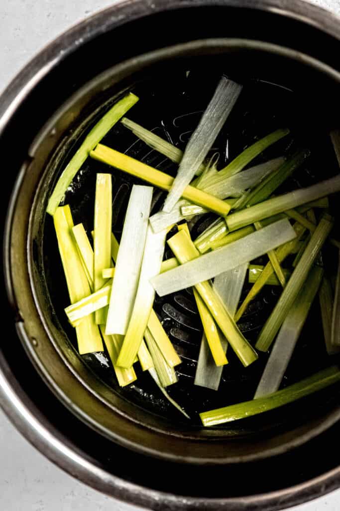 vertically sliced matchsticks of leeks that have been tossed in oil and salt and placed in the basket of an air fryer.