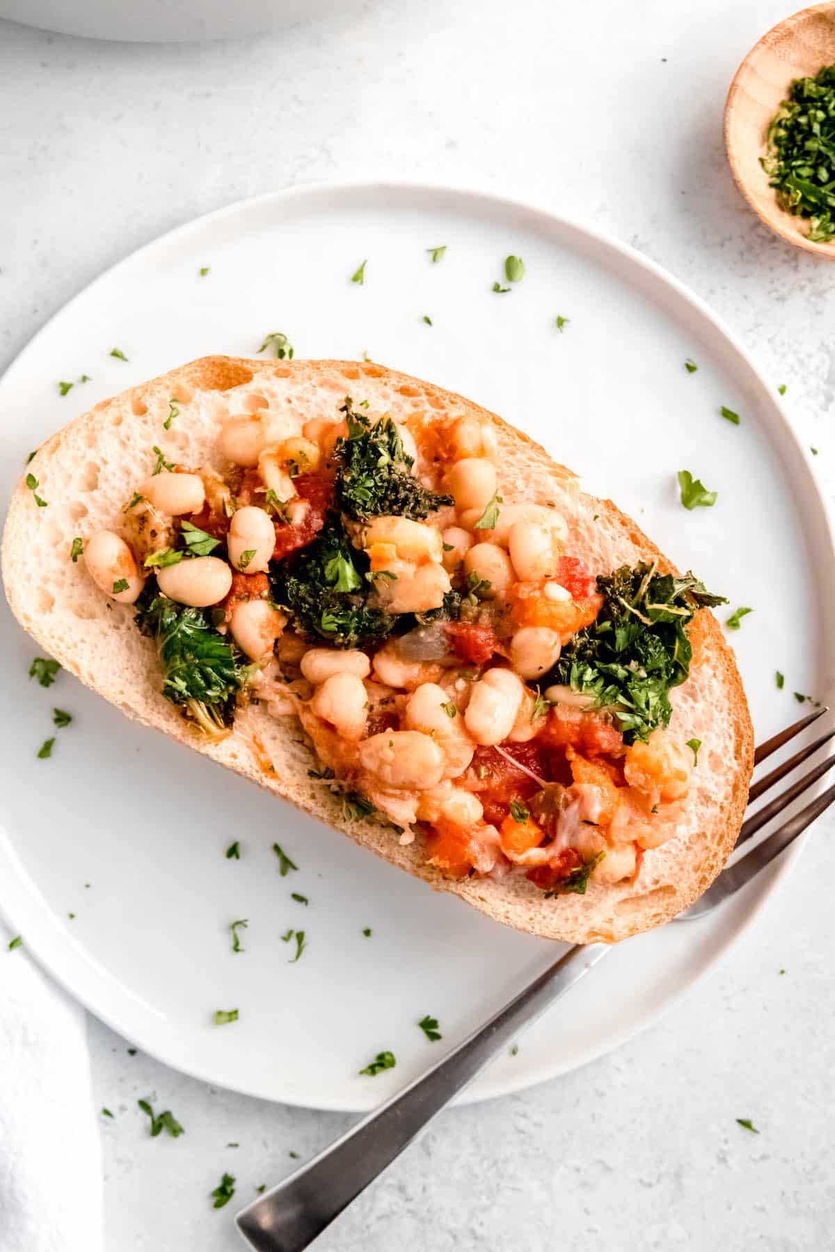 baked cheesy tomato white beans served on a slice of crusty butter toasted bread and sprinkled with fresh parsley.