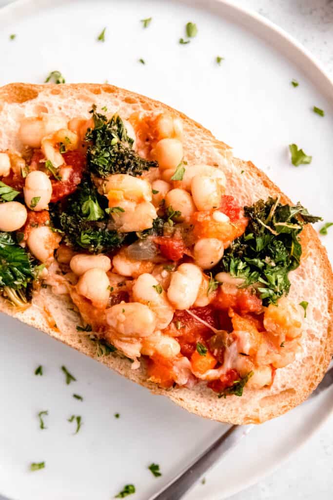 closeup shot of the cheesy tomato beans with kale served atop a slice of butter-toasted Italian bread.