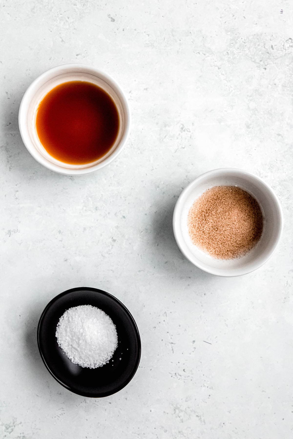 small bowls of vanilla extract, cinnamon sugar, and salt on a white table.