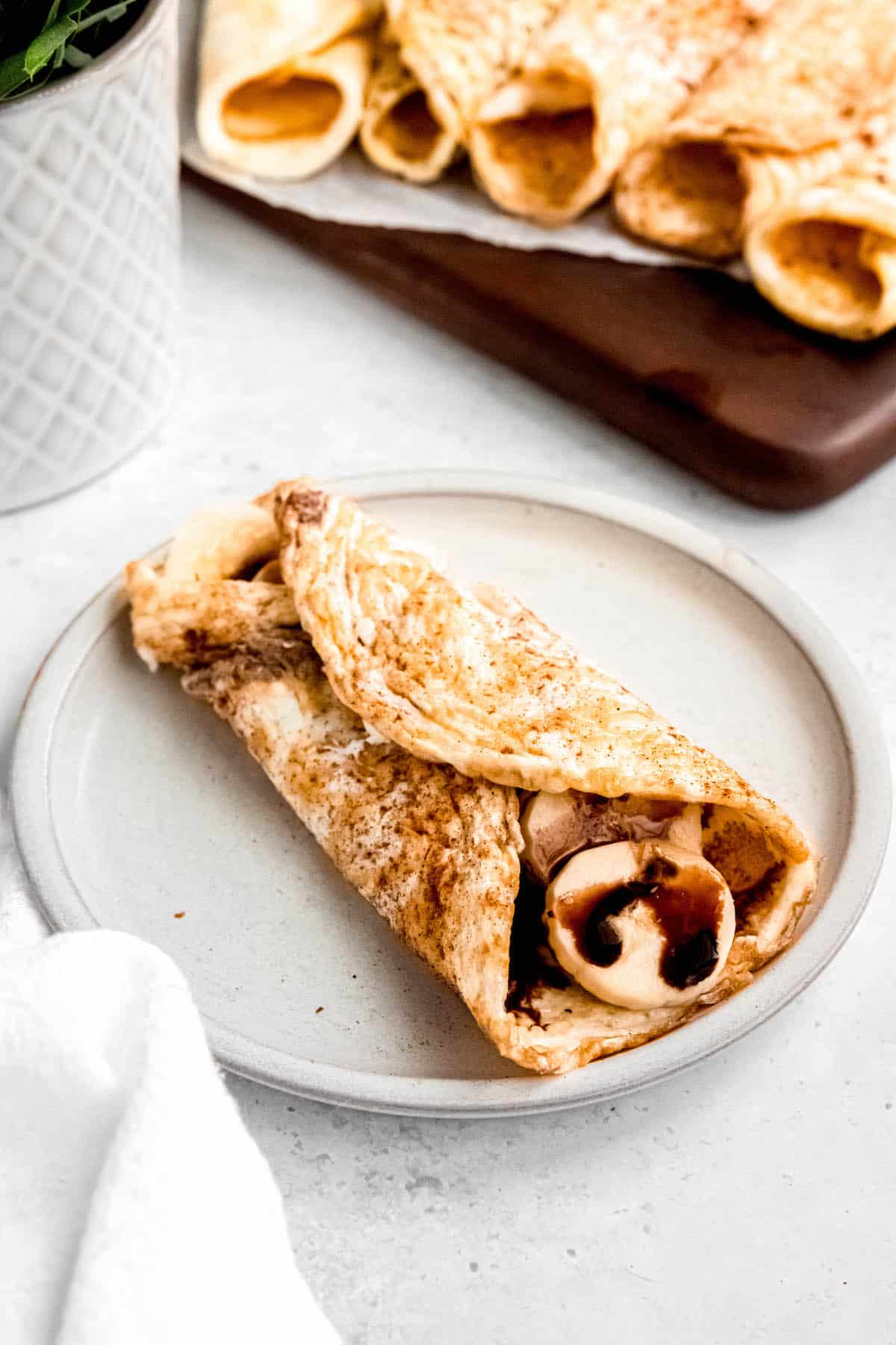 sweet cinnamon flavored egg white wrap rolled around banana and chocolate syrup like a sweet crepe on an earthenware plate.