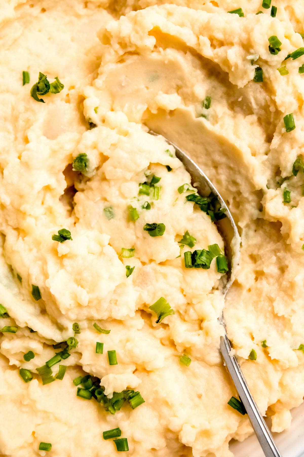 serving spoon scooping out a creamy pile of greek yogurt mashed potatoes that taste like sour cream and chive mashed potatoes, but healthier.