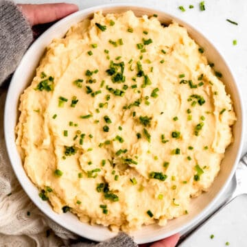 white bowl filled with greek yogurt mashed potatoes topped with chives.
