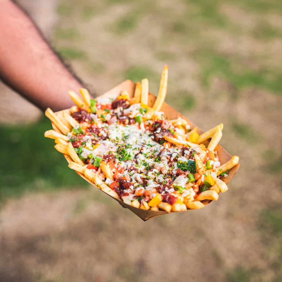 hand holding a tray of loaded french fries — potato bar idea.