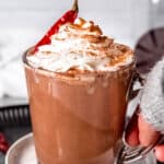 hand grabbing a spicy mexican mocha topped with whipped cream, cocoa powder and a dried chile.