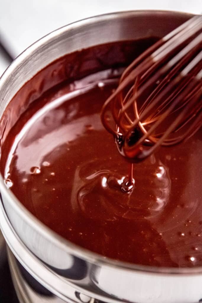 closeup of chocolate coffee ganache in the double boiler with some drizzling down from the whisk to show its viscosity.