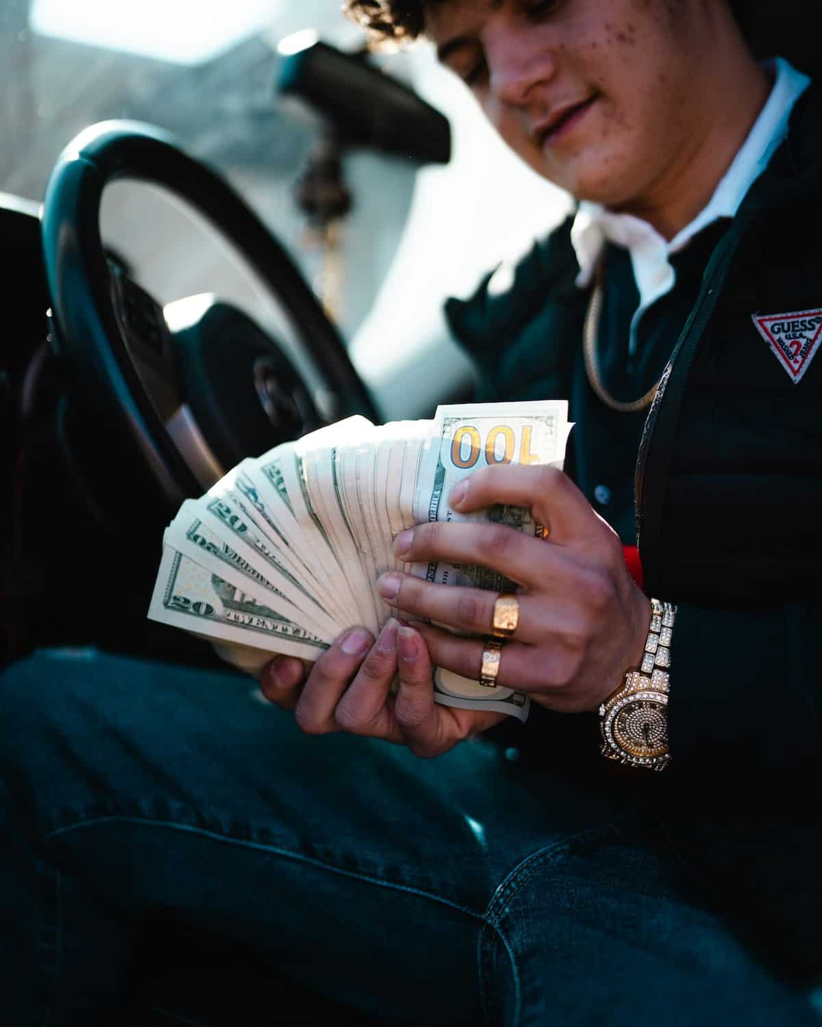 rich man in a car with hundreds in cash wearing designer clothes and gold jewelry.