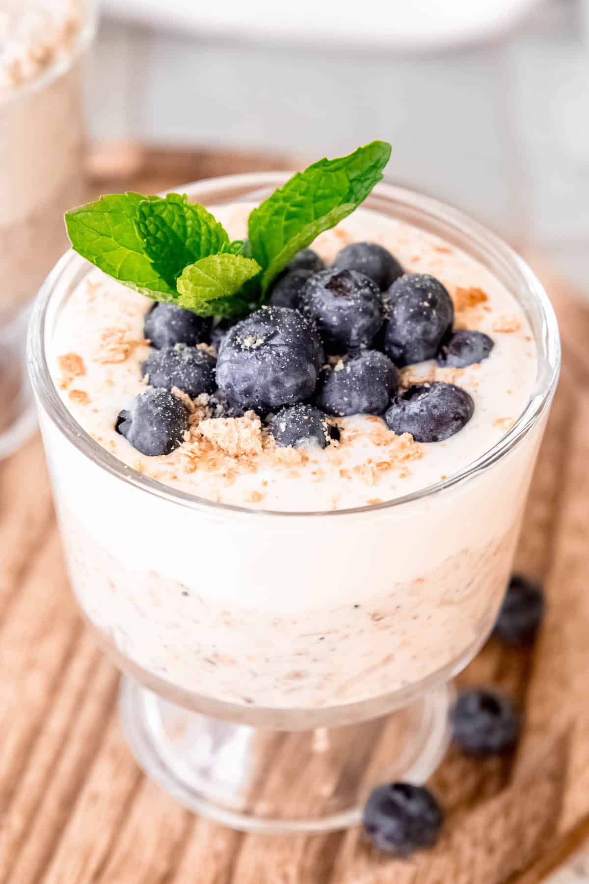 hero shot of a small trifle glass layered with overnight protein oats topped with a cottage cheese cheesecake layer, fresh berries, and graham cracker crumbs on a wooden tray with berries scattered around.