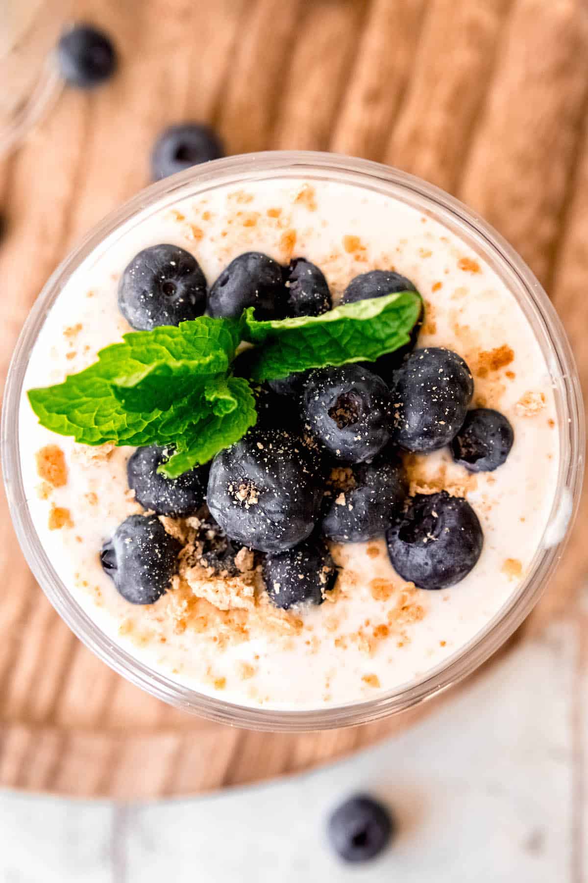 flat lay shot of the high-protein overnight oats showing the cheesecake layer topped with fresh blueberries, graham cracker crumbs, and a sprig of mint.