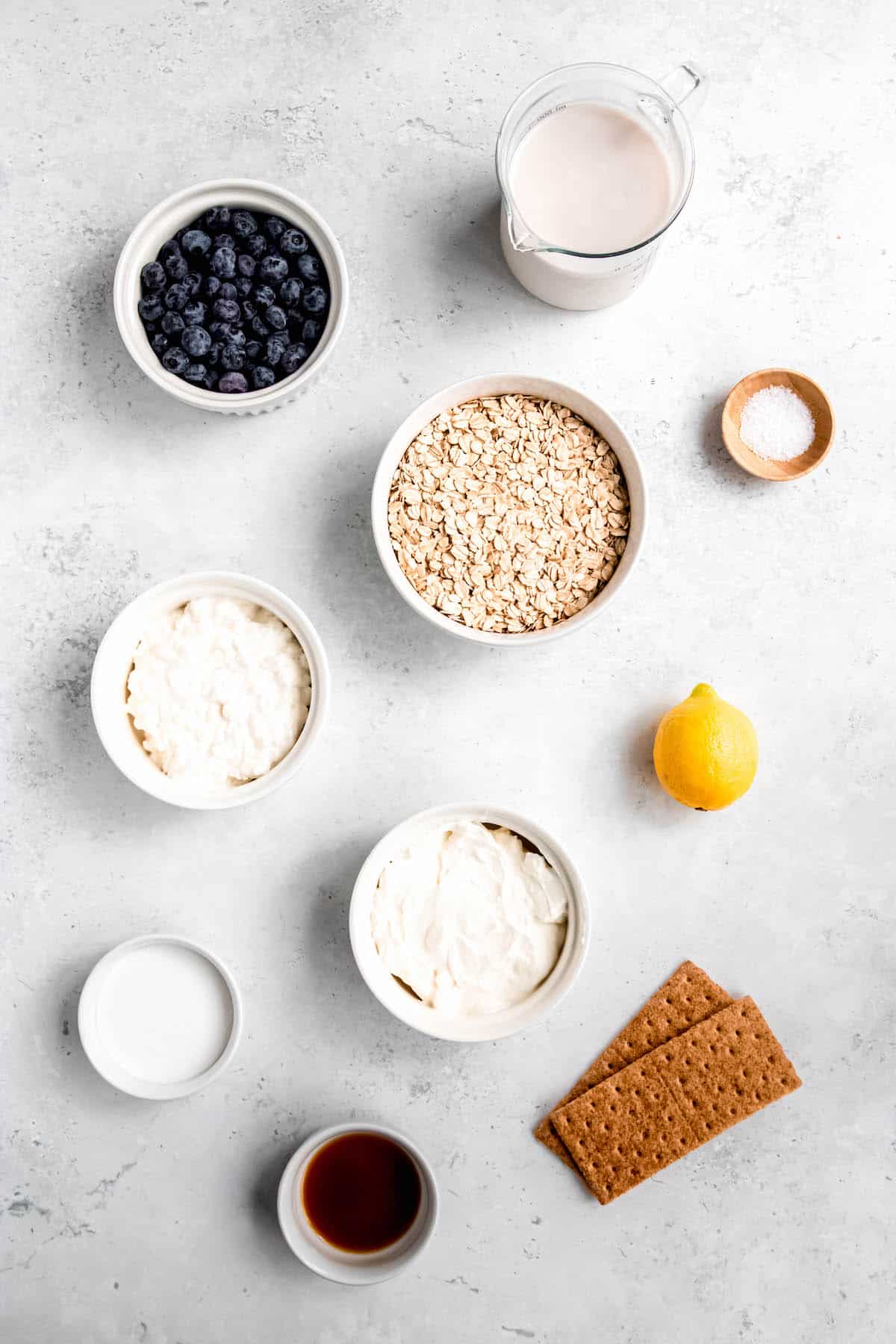 ingredients for making high-protein berry cheesecake overnight oats measured out into bowls on a white table.