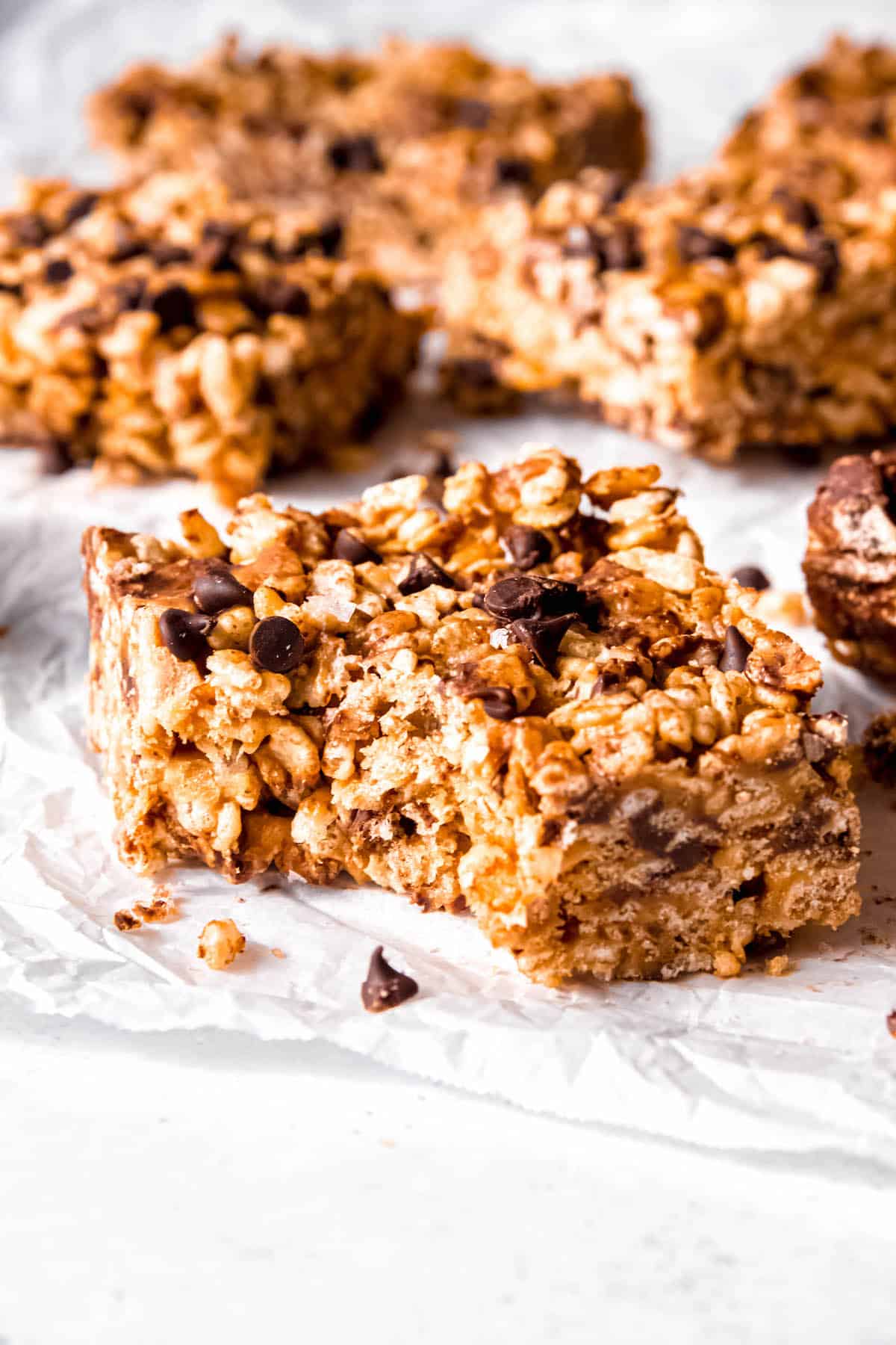 chocolate peanut butter rice krispies treats on parchment with the nearest one having a bite taken out.