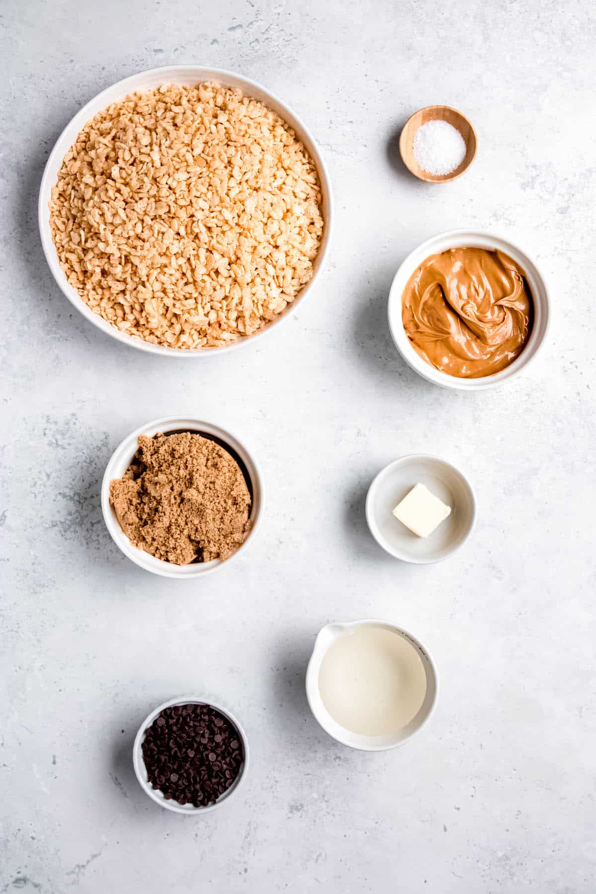 ingredients needed to make peanut butter chocolate chip rice krispies treats measured out into bowls on a white table.