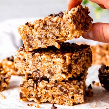 square hero image of a stack of 3 chocolate peanut butter rice krispies treats with a hand grabbing the top one from the stack.