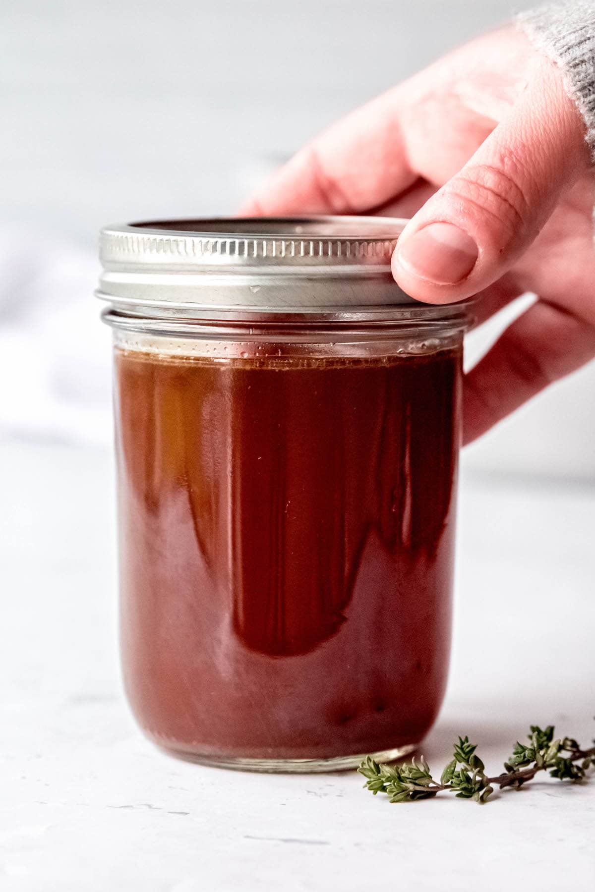 hand screwing a lid on a mason jar filled with homemade sipping broth made from scraps.
