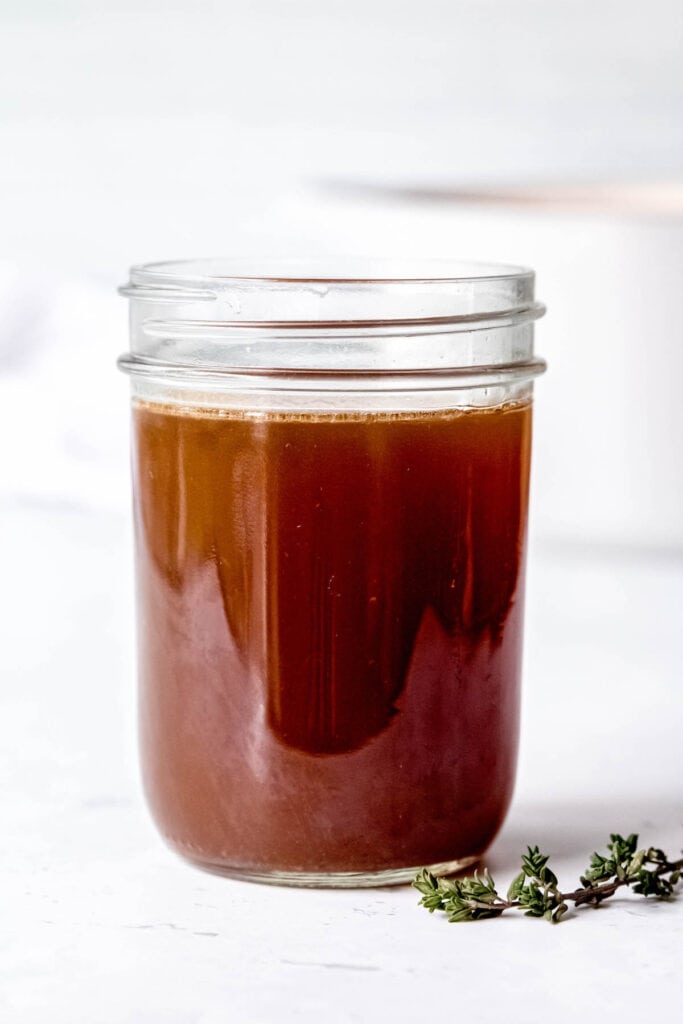 side on shot of a jar of dark brown roasted bone broth in a mason jar on a white table.