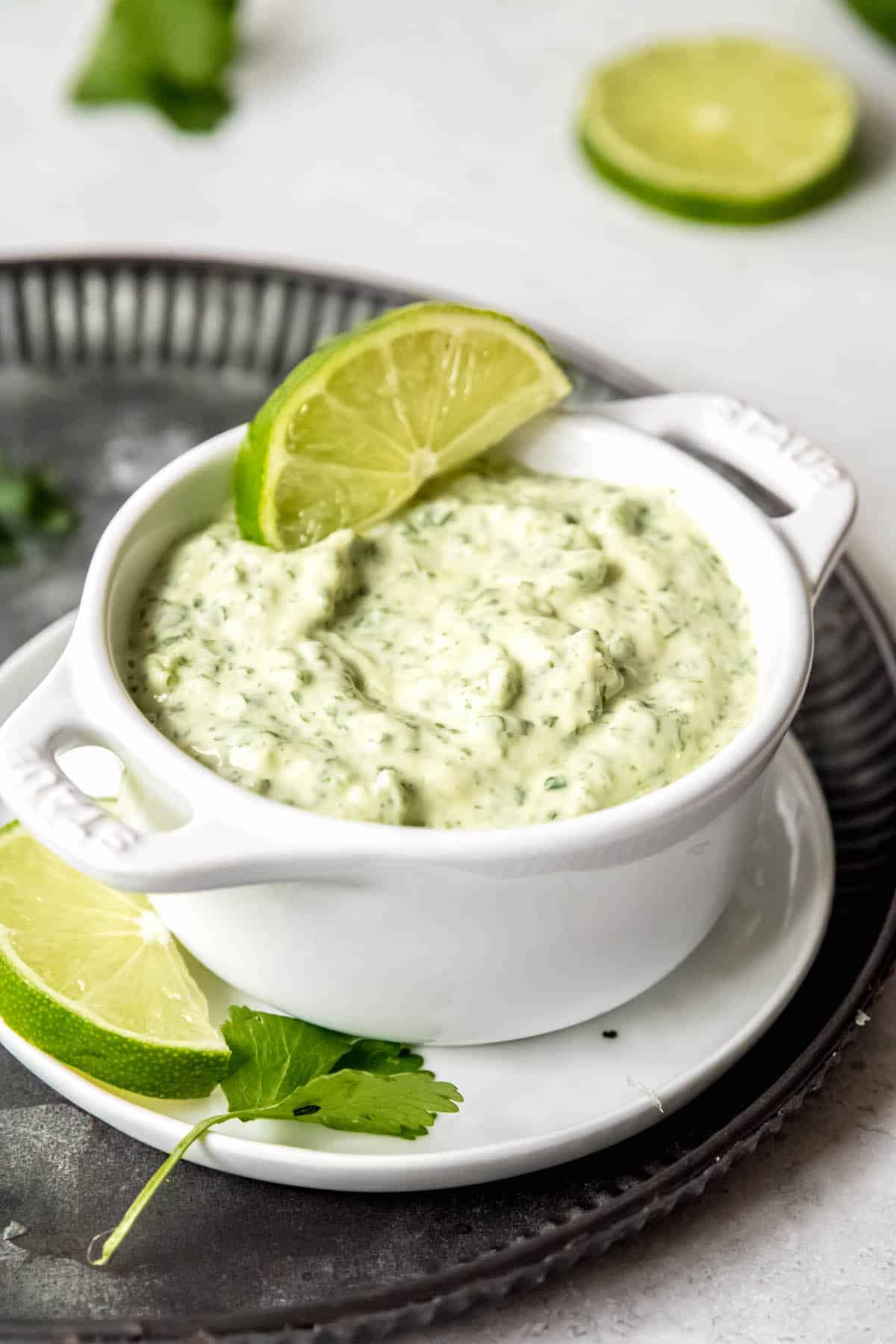 white dip bowl filled with creamy jalapeno garlic sauce with a sprig of cilantro.