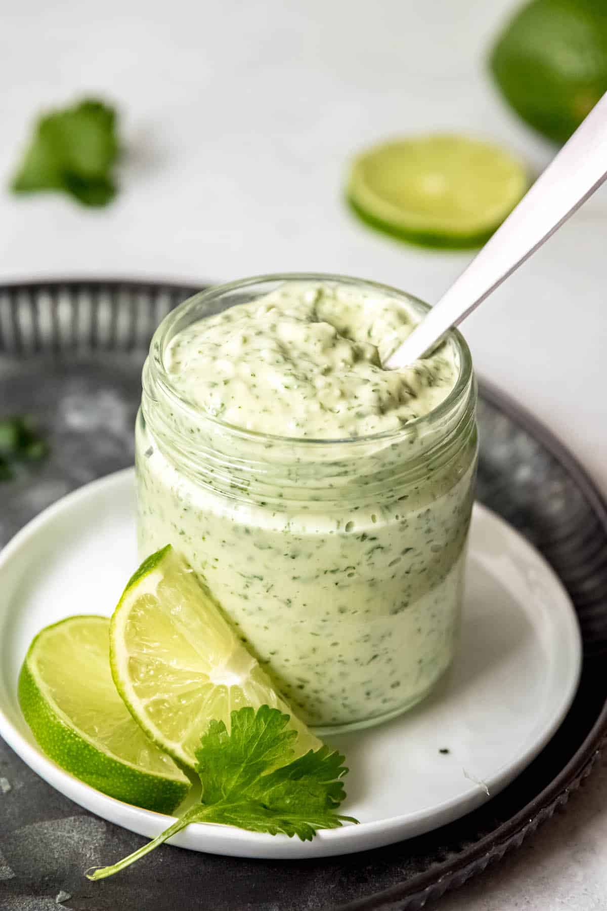 small glass jar filled with chuy's copycate creamy jalapeno cilantro lime garlic sauce with a silver spoon for serving.