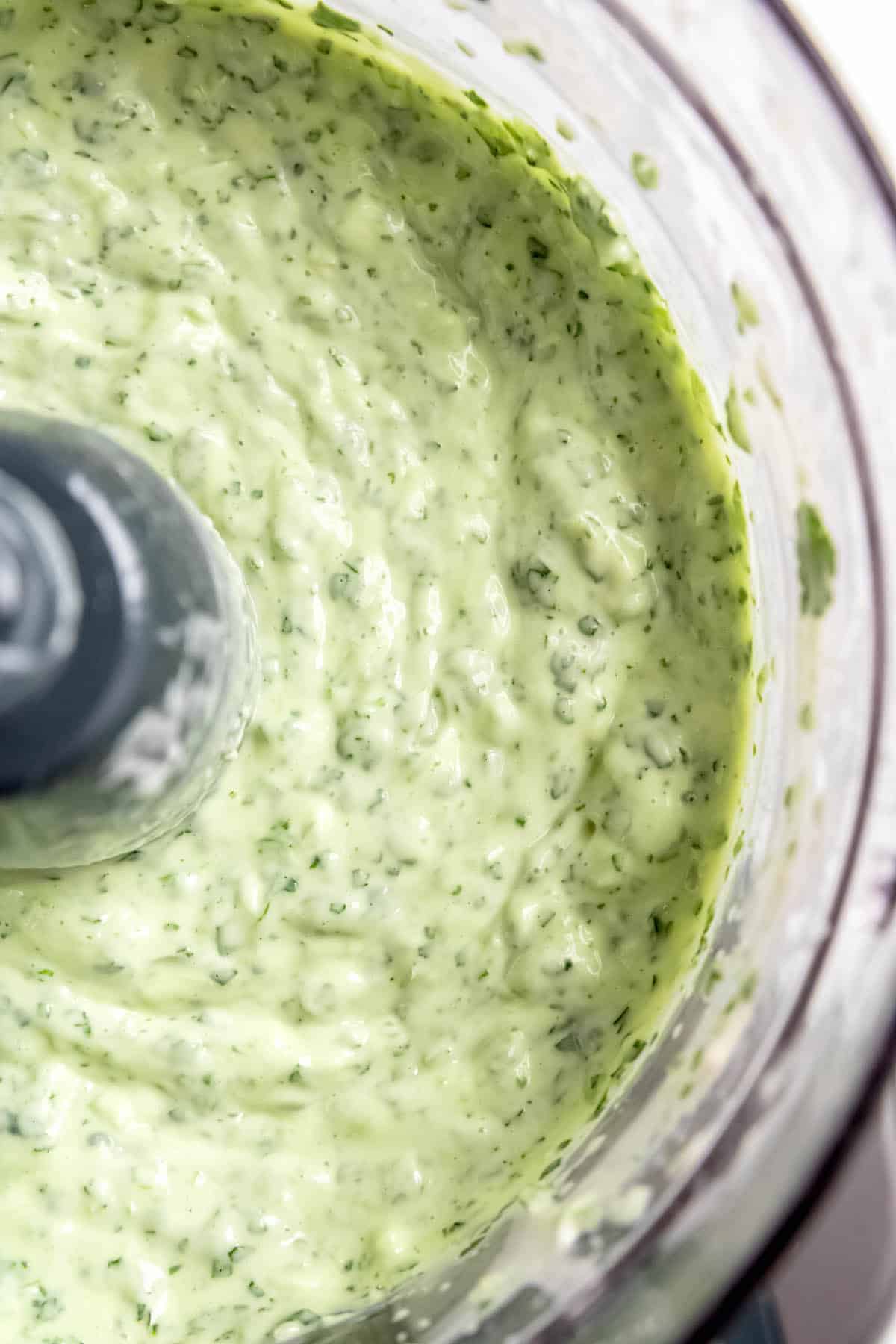 flat lay shot of creamy chimichurri cilantro sauce in the bowl of a food processor after blitzing.