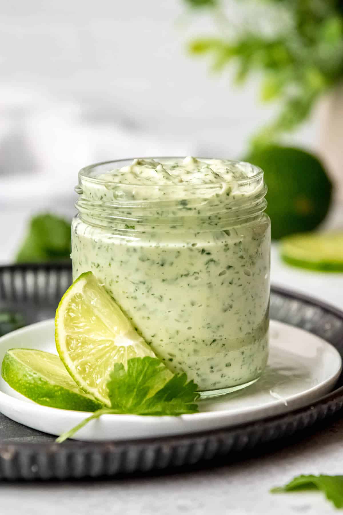 creamy jalapeno sauce with garlic, lime, cilantro and mayo in a small glass jar with slices of lime leaning against it.